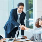 Four people, 2 men and 2 women meeting and shaking hands in business attire.