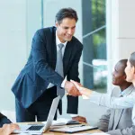 Four people, 2 men and 2 women meeting and shaking hands in business attire.