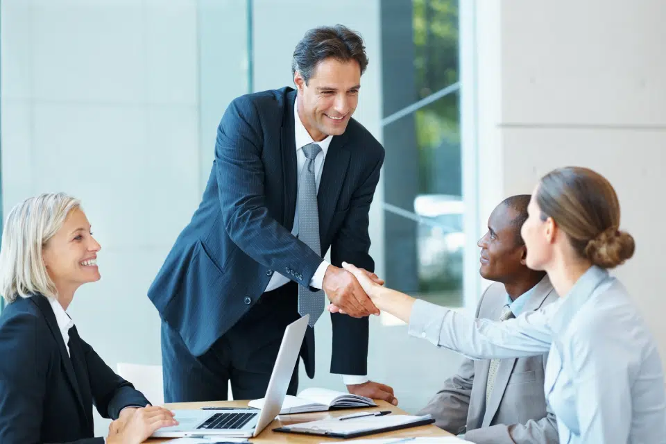 Four people, 2 men and 2 women meeting and shaking hands in business attire.
