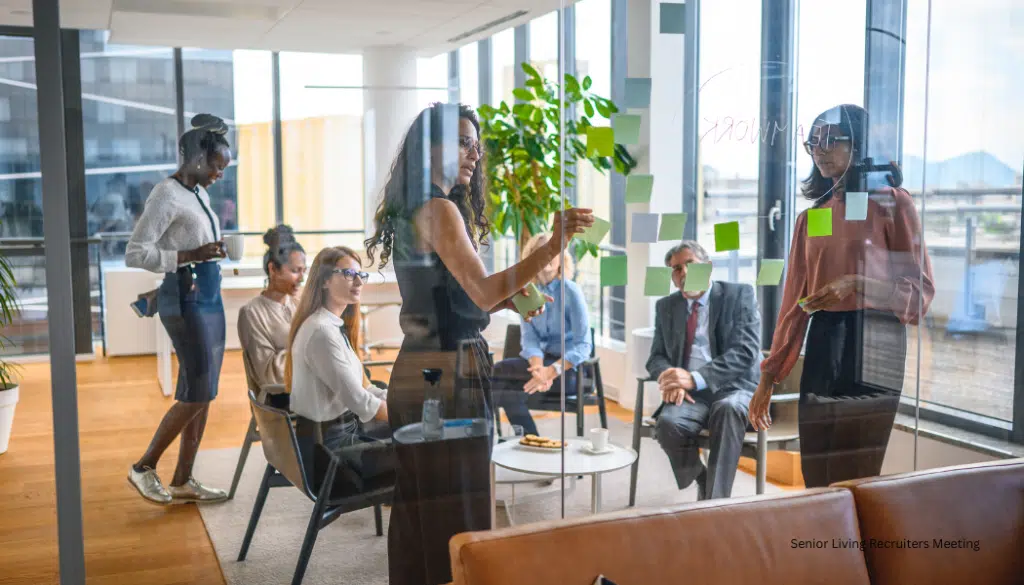 Senior Living Recruiters meet around a table in a conference room with windows