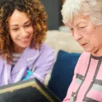 Female Memory Care Director looking at photo album with female resident in a courtyard