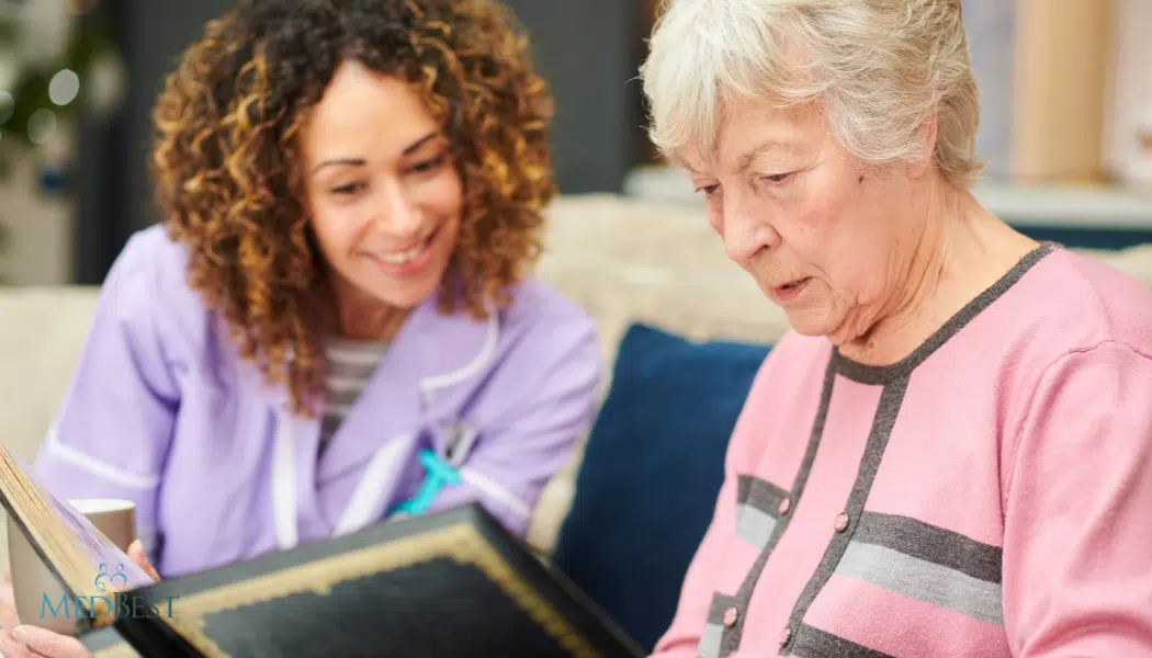 Female Memory Care Director looking at photo album with female resident in a courtyard