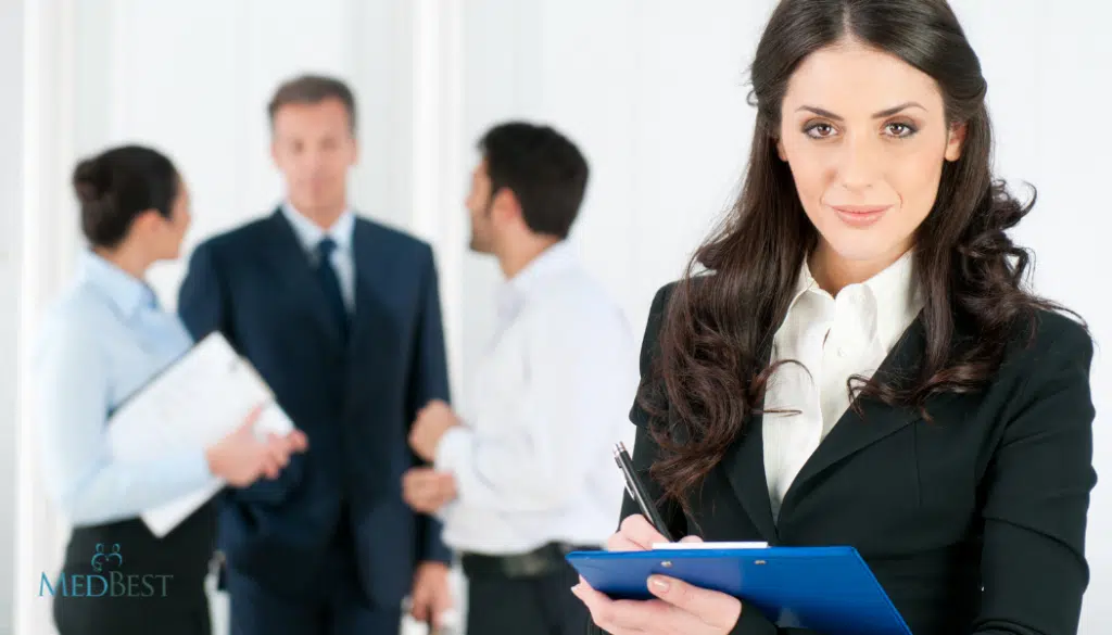 Female executive recruiter holding clip board is in front of three other recruiters having a brief office meeting