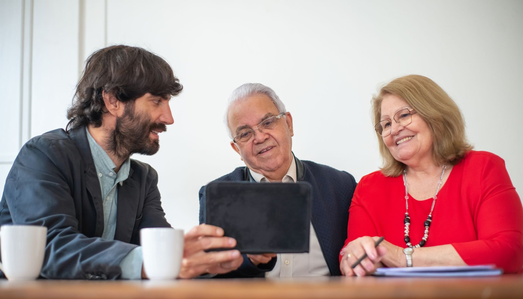 Adult son showing his senior parents information on a tablet at the kitchen table